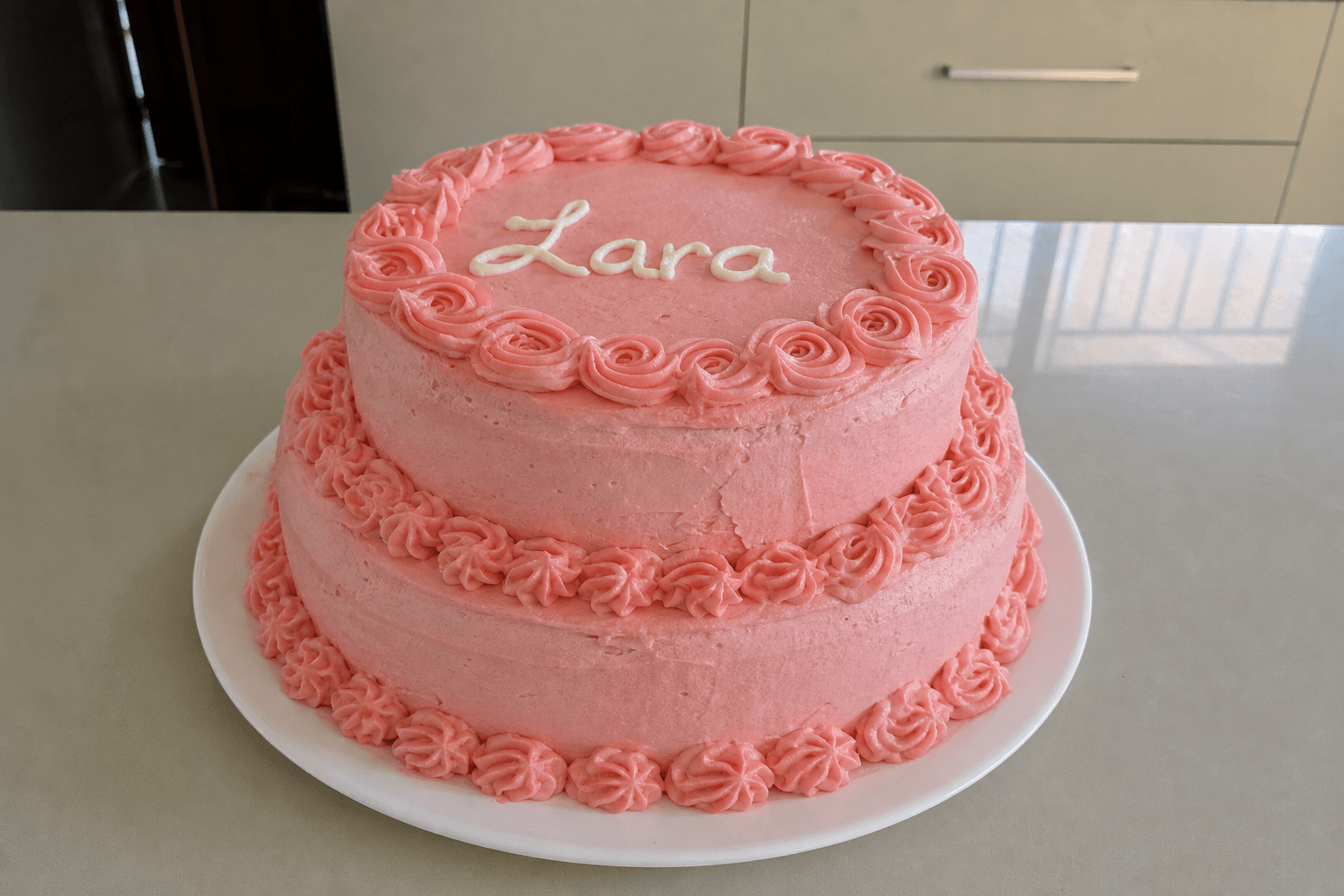 Bolo de aniversário de dois andares com cobertura rosa e o nome Lara escrito em glacé